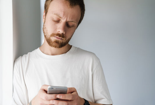 Photo of perplexed bearded man with red hair using mobile phone
