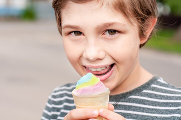 Fashionable boy eating multicolored ice cream in a waffle cone. Cool in the summer heat. Sweet snack. Hot Summer. Emotional child licks ice cream