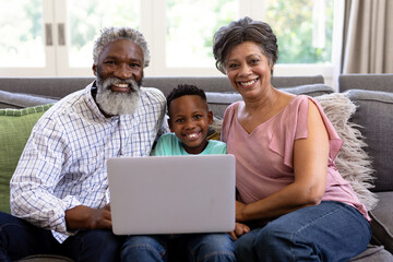 Mixed race boy and his grandparents using a laptop sitting on a couch