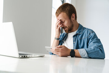 Naklejka premium Photo of man playing online game on cellphone while working with laptop