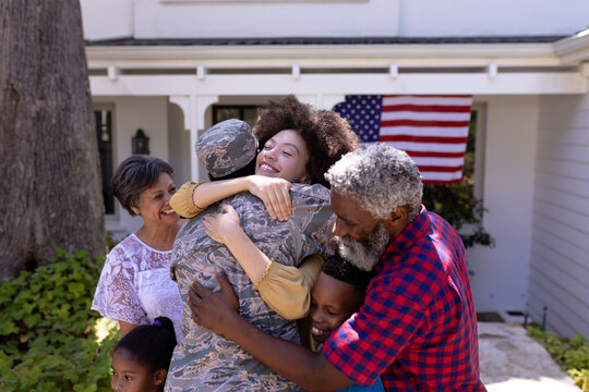 Multi-generation mixed race family welcoming an African American man wearing military uniform