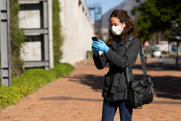Caucasian woman wearing a protective mask against coronavirus out in the streets, using her phone