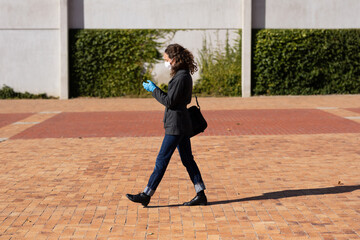 Caucasian woman wearing a protective mask and gloves walking in the streets, using her phone