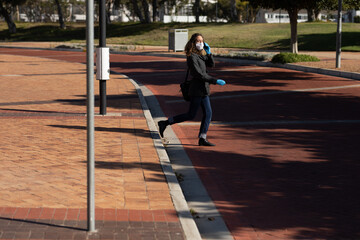 Caucasian woman wearing a protective mask and gloves walking in the streets, using her phone