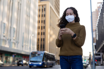 Caucasian woman wearing a protective mask and using her phone in the streets