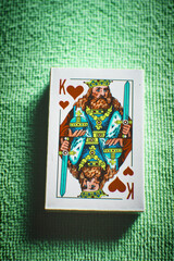 A deck of new cards in a paper box on a green table, the king of spades, top view.