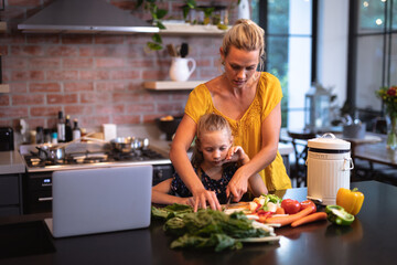 Caucasian woman and her daughter spending time in the kitchen and using a laptop