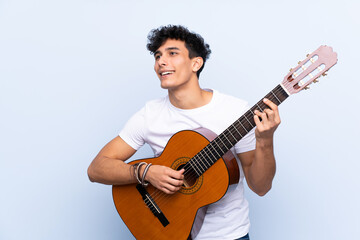 Young Argentinian man with guitar over isolated blue background