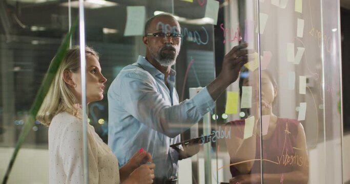Professional businesspeople discussing together and sticking a memo note on the glassboard in modern