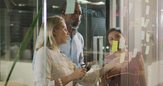 Professional businesspeople discussing together over a glassboard in modern office in slow motion