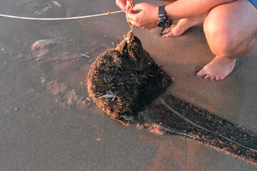 Untying small trawling net with catch of the day for fishing along the beach