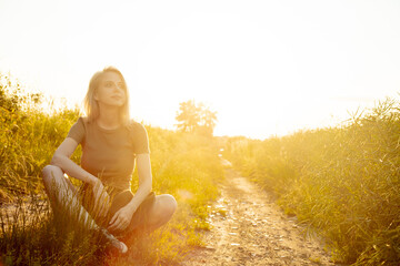 beautiful blonde girl is sitting on countryside road during sunset