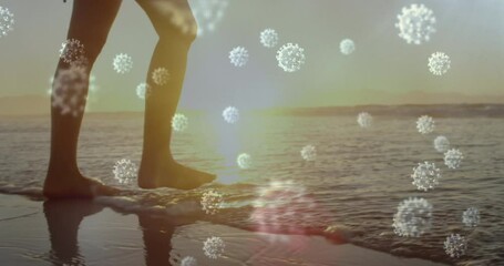 Digital composite video of covid-19 cells moving against low section of woman walking on the beach - Powered by Adobe