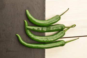 Green chili pepper, close-up, on a slate board and white wooden table.