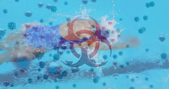 Digital composite video of hazard sign with covid-19 cells moving against woman swimming in a pool