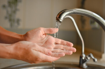
Washing hands with soap near the tap. Water pours from the tap.