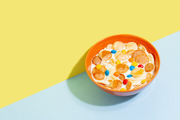 Orange bowl with tiny pancake cereal porridge with milk on a blue yellow background copy space.Trendy tasty breakfast food