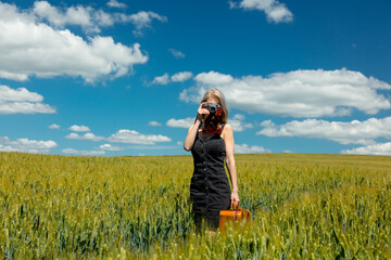 Beautiful blonde girl with suitcase and vintage camera in wheat field in sunny day