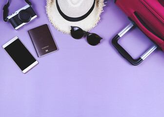 flat lay of traveler accessories , passport , hat , mobile phone, camera,sunglasses and pink suitcase on purple background. travel concept.