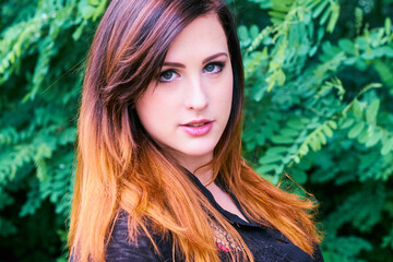 Sensual smiling young woman with gray eyes and an ombre hairstyle mix of dazzling color tones, wearing a silver nose ring and glancing sensually into camera at a green park.