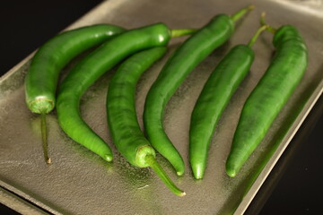 Green chili peppers on a metal tray, on a black background.