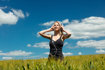 Blonde woman with headphones in wheat field in sunny day