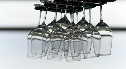 Many empty crystal wine glasses hanging upside down on a special rack over the counter of a bar.