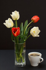 Fototapeta na wymiar Bouquet of yellow tulips in vase with cup on a black background.