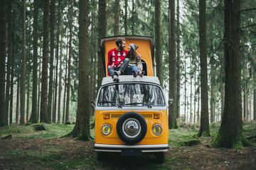 Traveler couple embracing and resting in forest on Orange retro Bulli Vintage Camper.