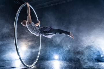 Cyr Wheel circus artist on smoked, dark background performing on stage 