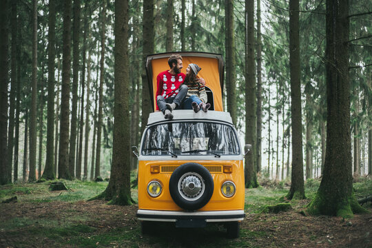 Traveler Couple Embracing And Resting In Forest On Orange Retro Bulli Vintage Camper.