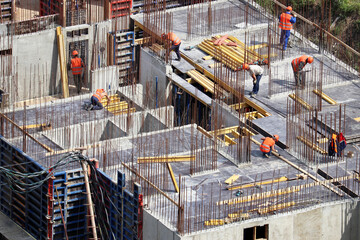 Workers laying concrete floors and building walls on construction site. House development,...