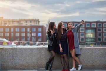 Charming women are posing while making photo with cell telephone digital camera during their free time in weekend. Pretty hipster girls are shooting video on smart phone during walking tour outdoors