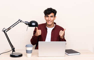 Young Argentinian man in a table with a laptop in his workplace giving a thumbs up gesture