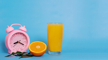 Closeup pink alarm clock with glass of orange juice and fresh ripe fruit on a blue background. Organic breakfast concept