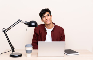 Young Argentinian man in a table with a laptop in his workplace laughing and looking up