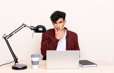 Young Argentinian man in a table with a laptop in his workplace thinking an idea