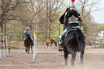 A knight in vintage armor of the 15th century rides a horse across a field for a tournament