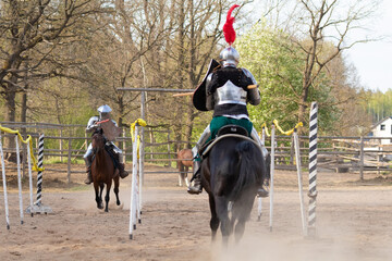 A knight in vintage armor of the 15th century rides a horse across a field for a tournament