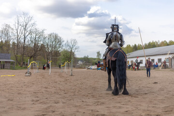 A knight in vintage armor of the 15th century rides a horse across a field for a tournament