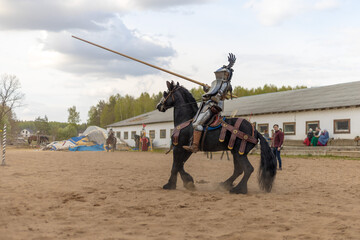 A knight in vintage armor of the 15th century rides a horse across a field for a tournament