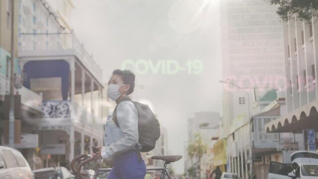 Animation of words Covid-19 floating over Asian woman wearing mask on a street with a bike