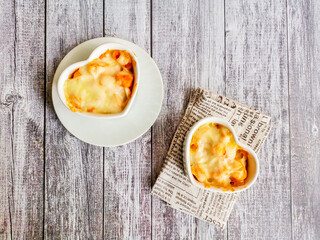 Top view macaroni and cheese in white heart shape bowl on wooden table with copyspace. Homemade...