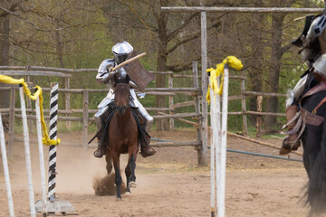 A knight in vintage armor of the 15th century rides a horse across a field for a tournament