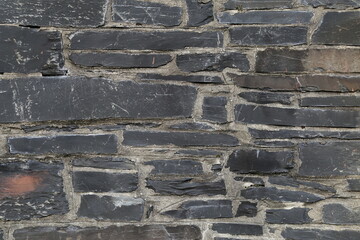 A closeup view of a wall constructed of grey Welsh slate with non uniform stones and mortar.
