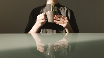 Diet concept: a young woman in a gray T-shirt holds in her hands a coffee cup with a cactus. The fight against excess weight and extra pounds.