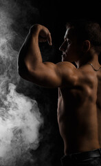 Fototapeta na wymiar Muscular young man from the back on a black background with smoke
