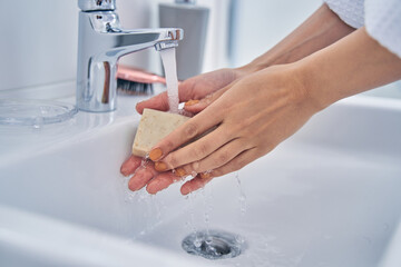 Young woman washing hands with soap in bathroom