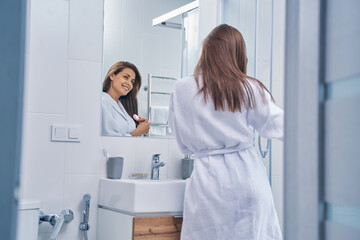 Cheerful young woman brushing hair in bathroom