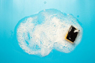 Soap foam from a cleaning agent and a cleaning sponge on a blue background. Cleaning concept,...